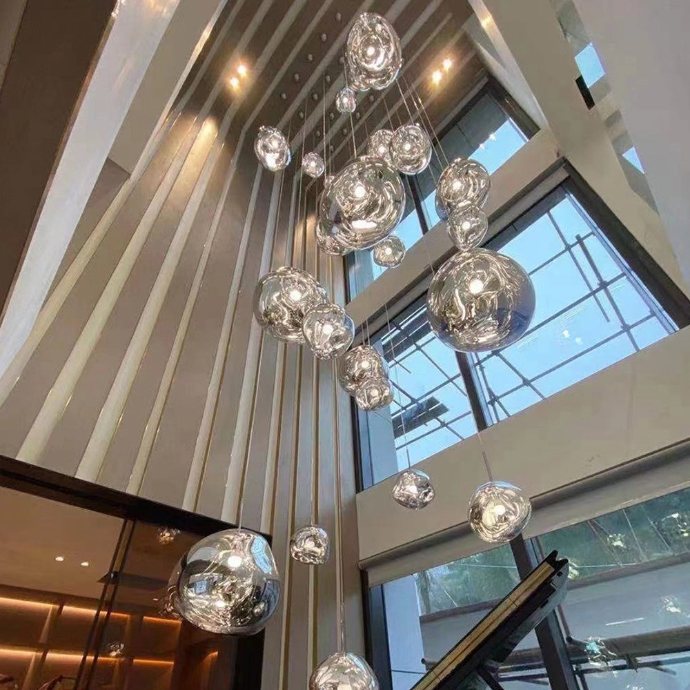 Silver irregular shades on staggered drops in a tall stair hall beside vertical wood slats and black stairs