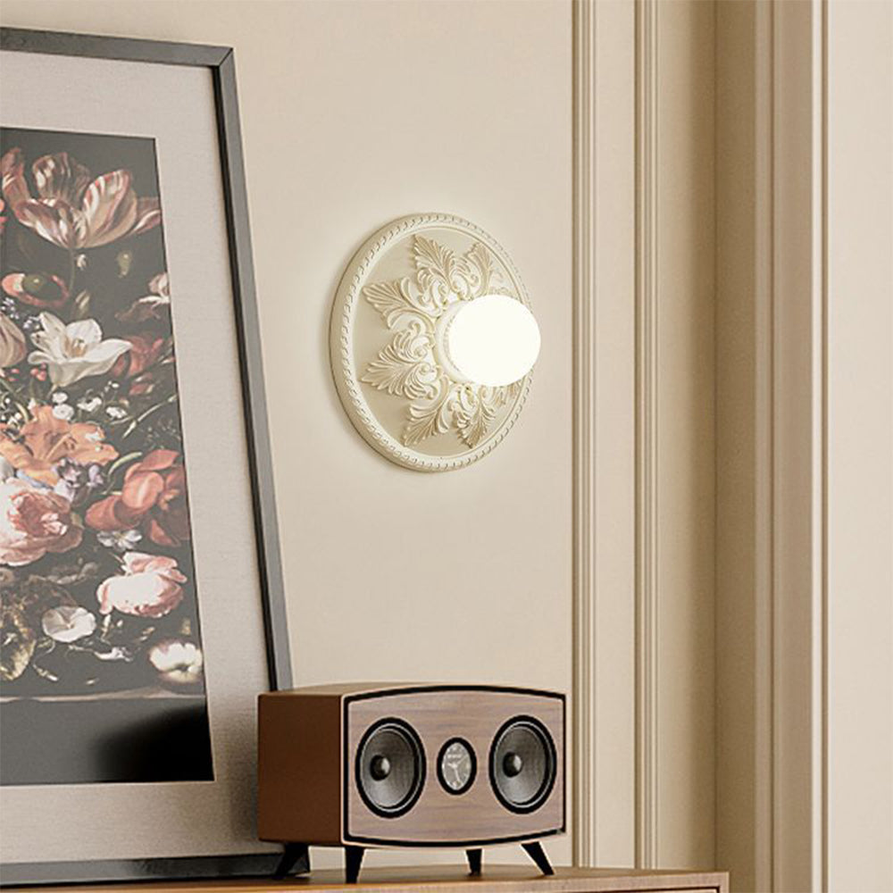 Cream globe wall light beside framed floral artwork and wood-cased speaker on a cabinet