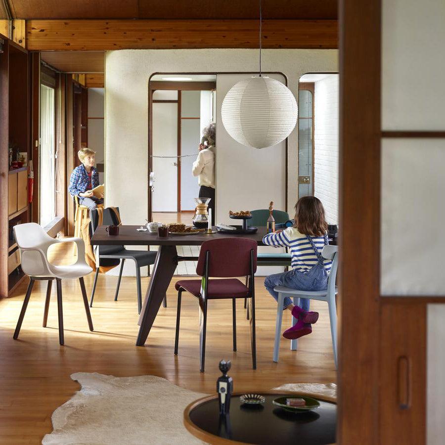 Paper globe above a dark wood dining table with colourful chairs in a timber-walled room