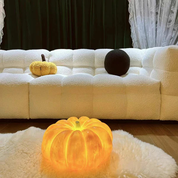 Glowing pumpkin lamp on a white shaggy rug before a white tufted sofa with pumpkin and round cushions