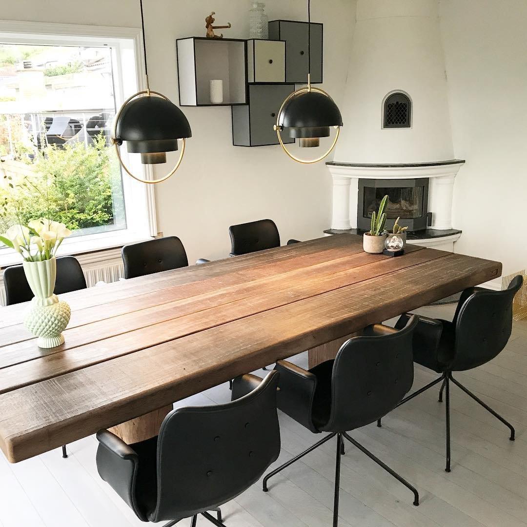Black dome pendants above a long wooden dining table near a garden window.