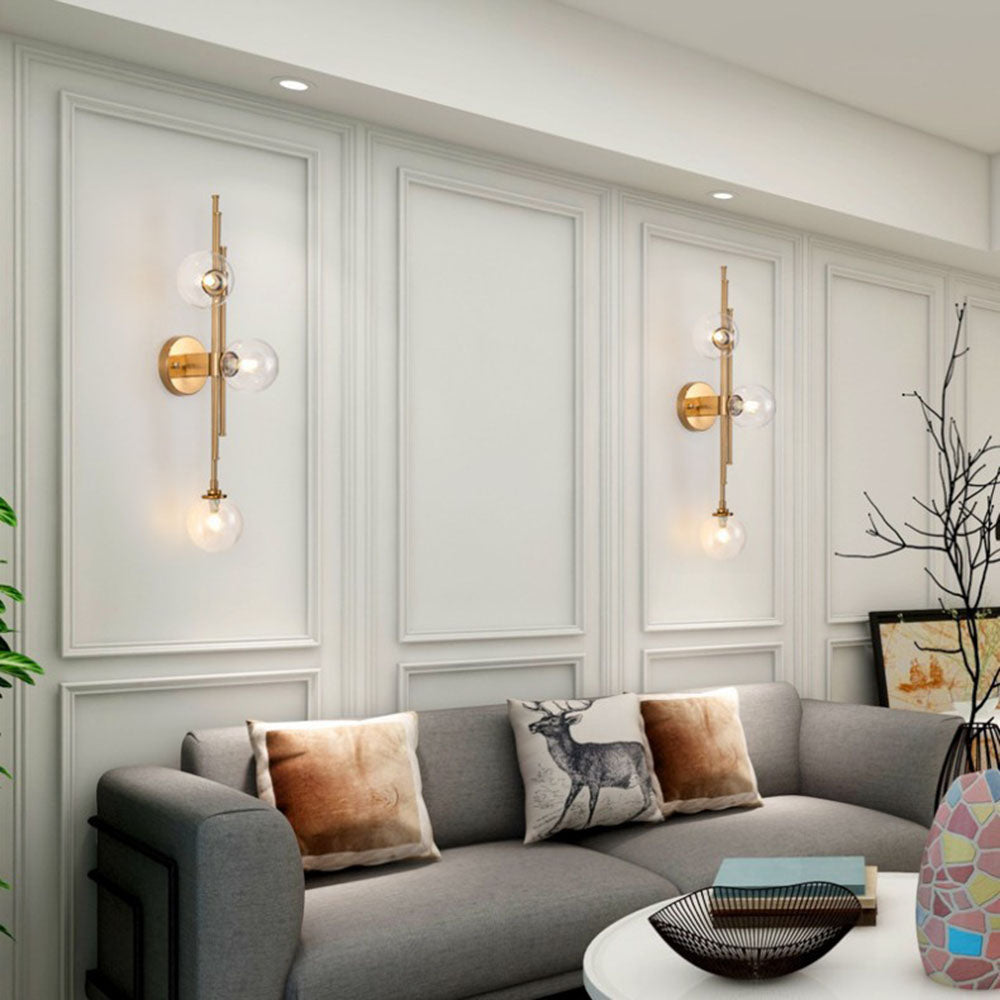Two clear-globe wall lights in white wall panels above a grey sofa with tan and deer-print cushions