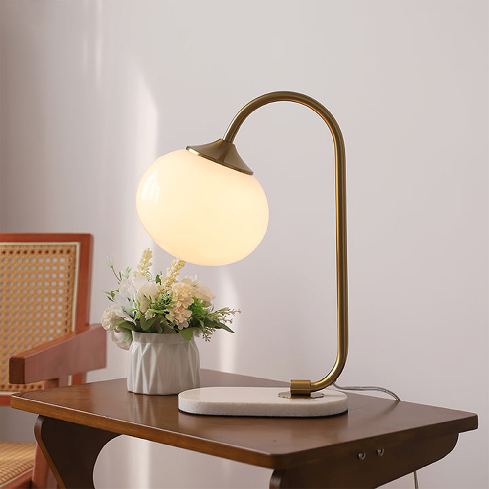 Glowing beige globe lamp with a gold-tone stem beside a flower vase and cane-backed wood chair