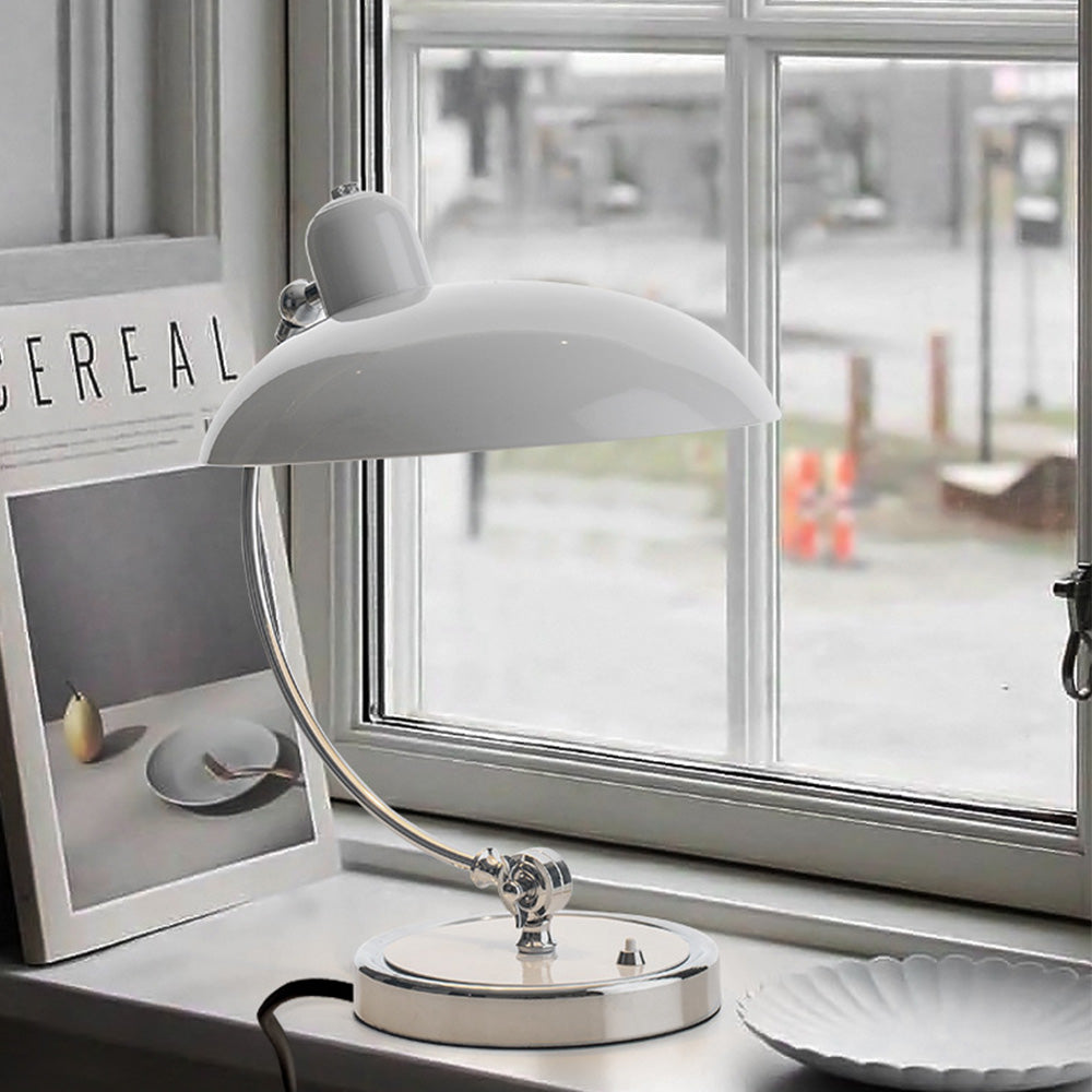 White curved-stem lamp on a window ledge beside a magazine and shallow fluted bowl