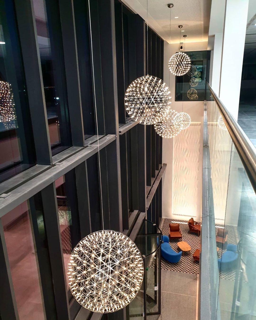 Globe pendants in a glazed atrium with coloured chairs, a balustrade and reflections