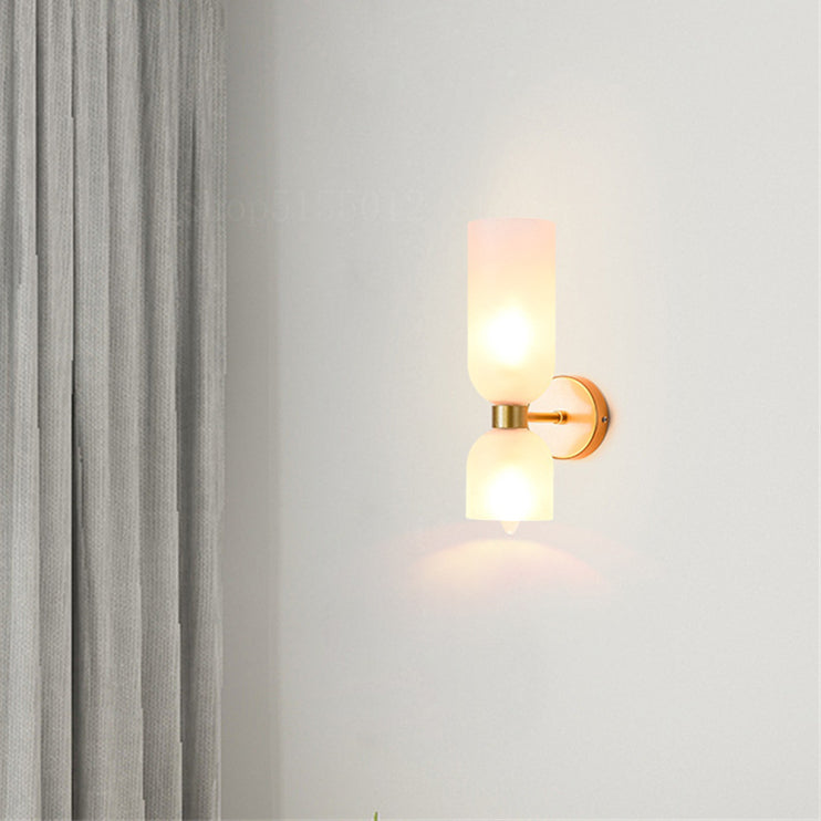 Lit White wall sconce in side view with gold-tone housing and lower bulb tip near a grey curtain