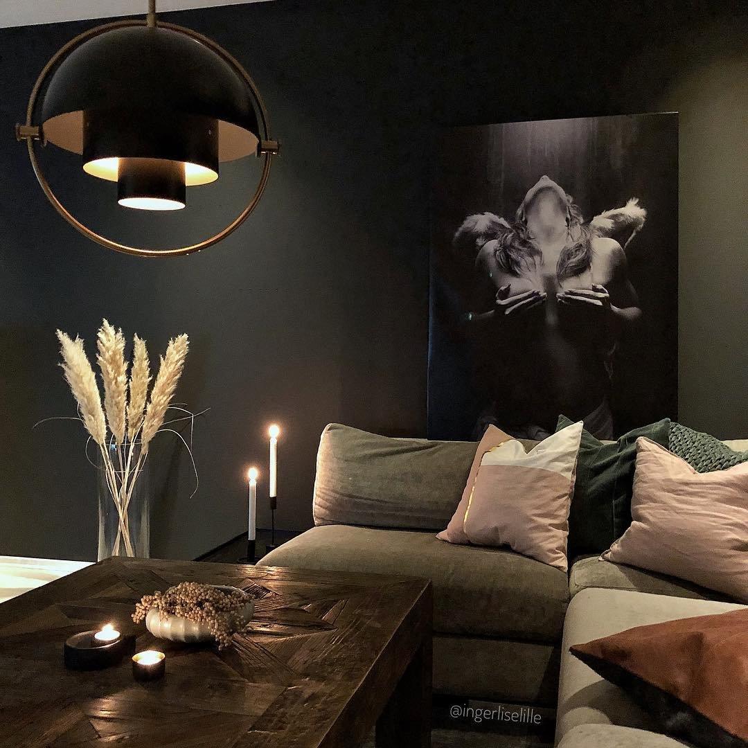 Illuminated black-and-gold pendant above a sofa and tabletop candles.