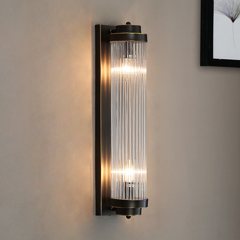 Lit Black Crystal Pillar wall light on a warm beige wall beside framed botanical artwork
