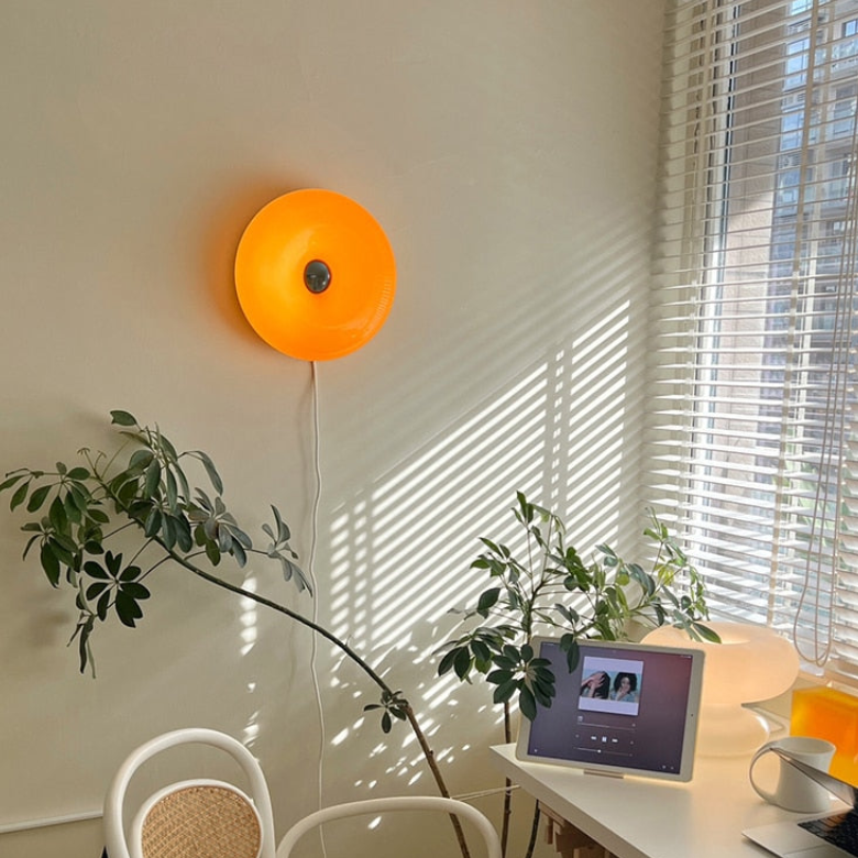 Orange donut light by window blinds and plants above a desk with tablet, mug and white chair