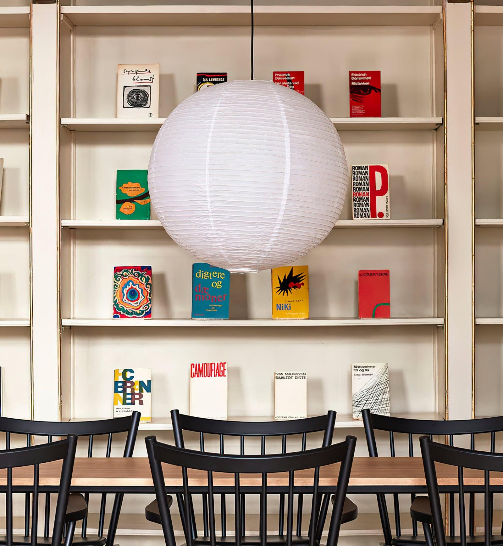 White globe before a cream bookshelf with gold rails above a wood table and black spindle chairs