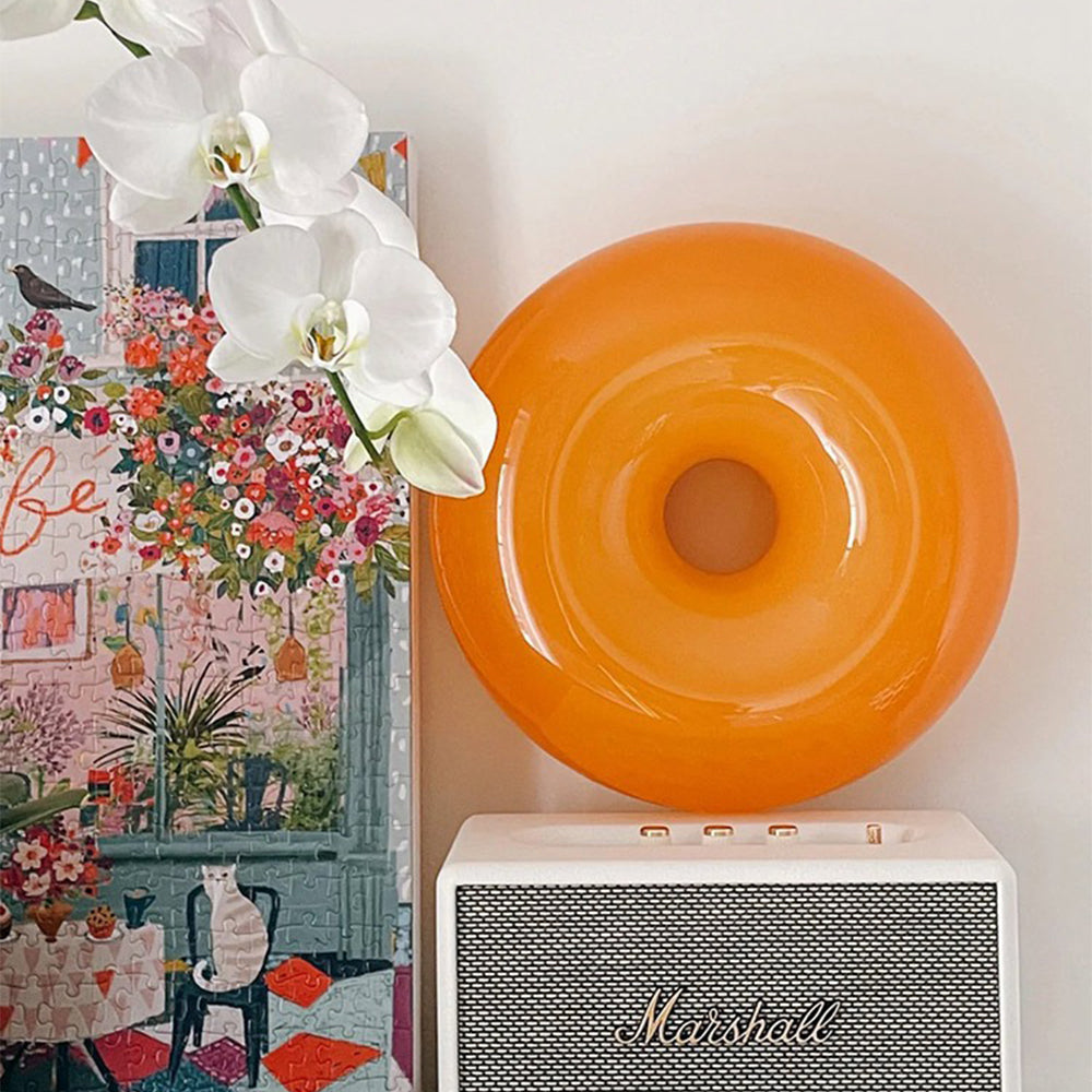 Orange donut wall light beside white orchids and colourful art above a speaker
