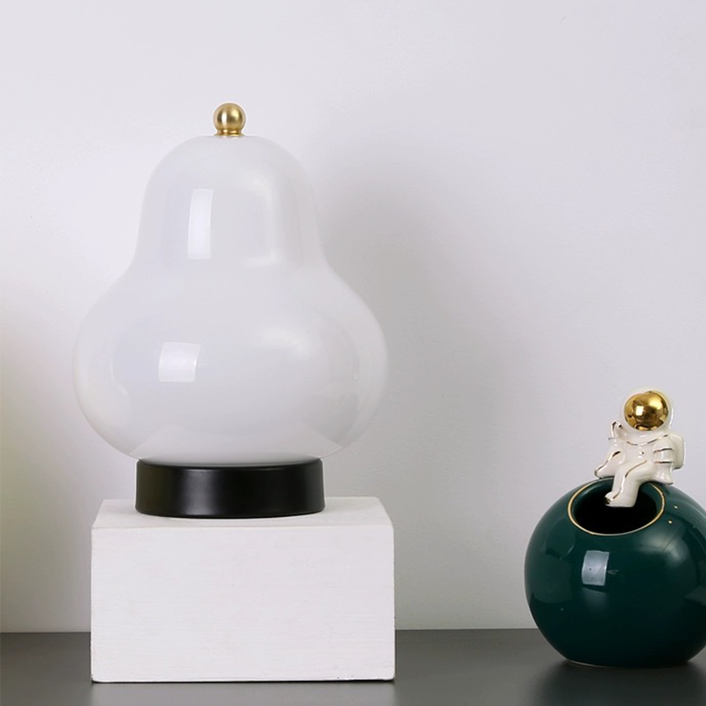 Unlit glossy white pear-shaped lamp on a white cube beside a dark green vase topped by an astronaut ornament