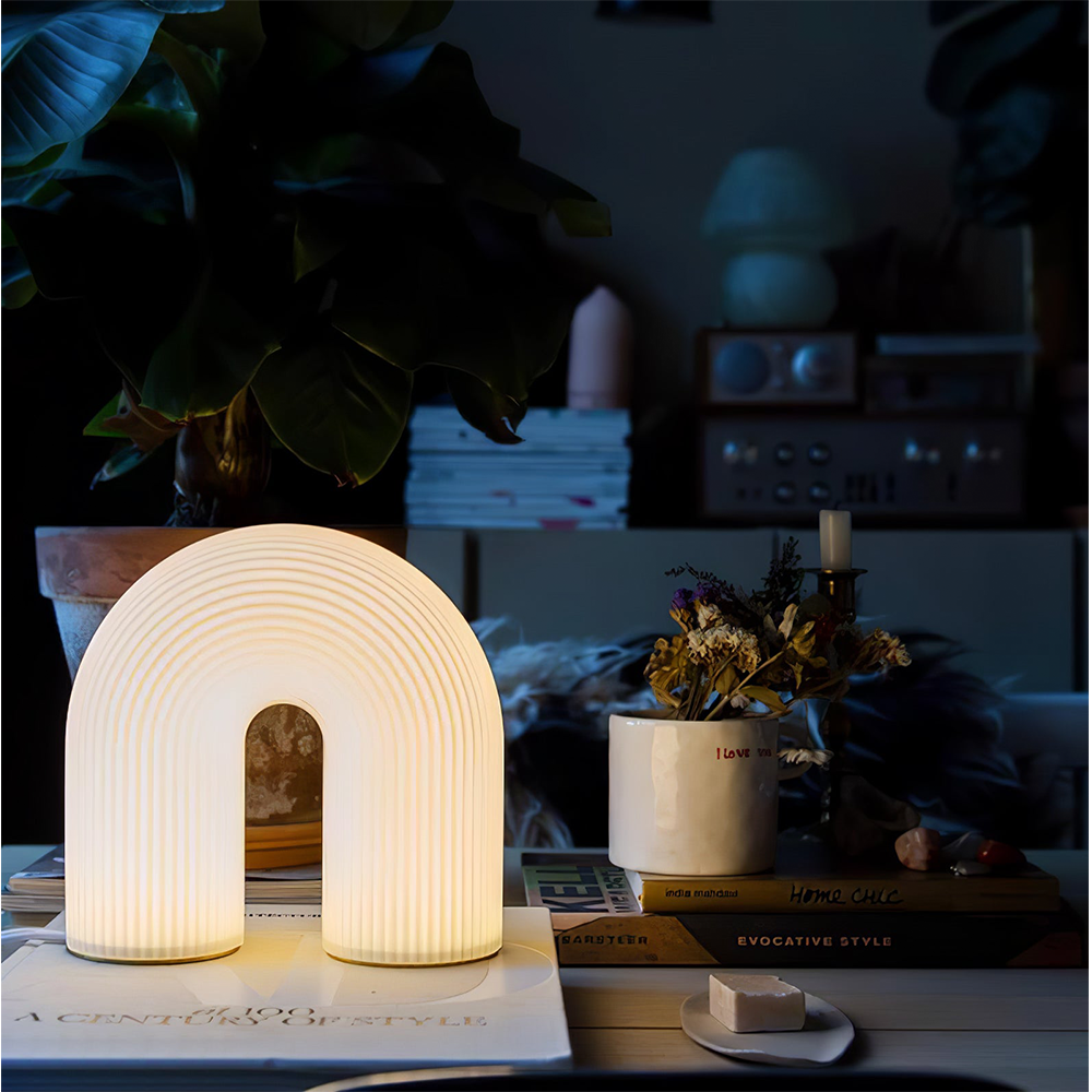 Glowing Arch lamp on art books beside a cup of dried flowers and a candlestick in a dark room