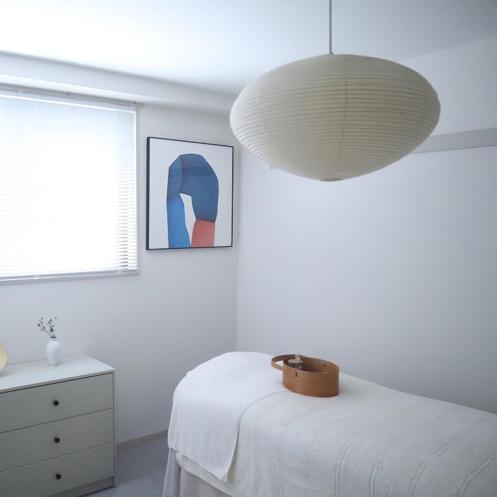 White paper pendant above a white-covered surface with a wooden basket beside drawers and blue abstract art