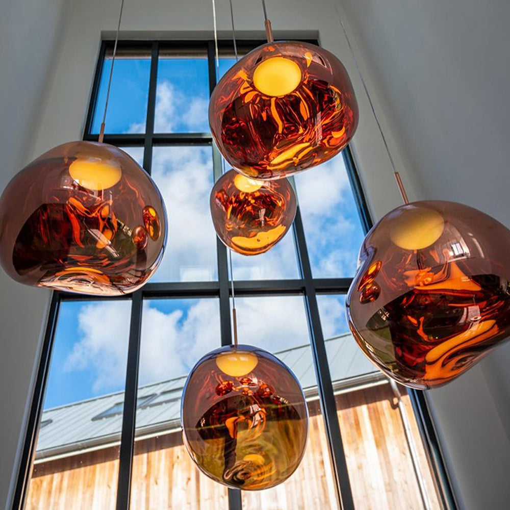 Five glowing Rose Gold irregular pendants on staggered drops against a tall window and blue sky