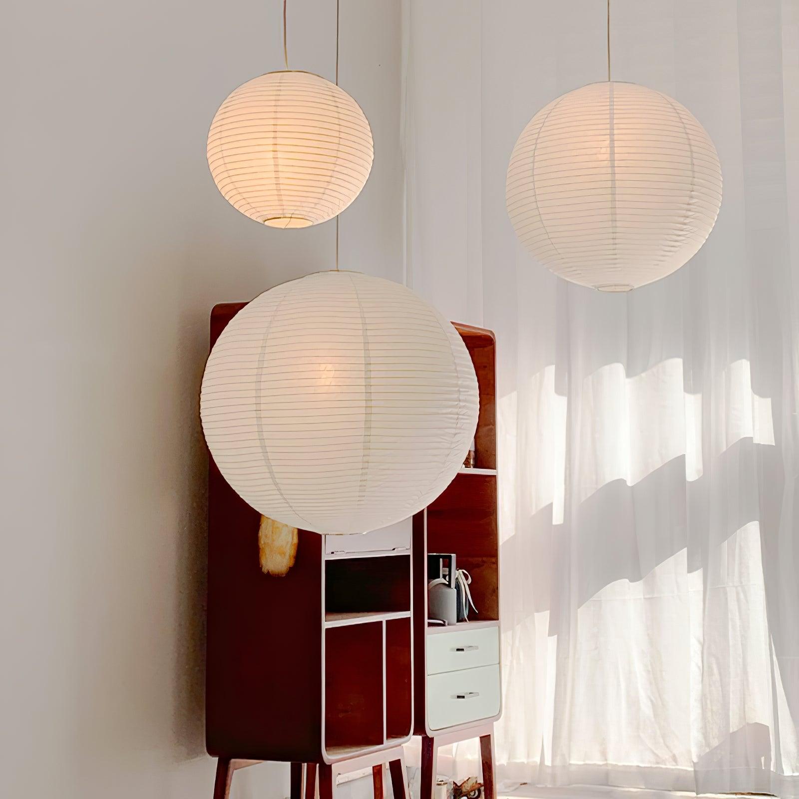 Three White paper globes in sunlight above a red-brown cabinet before sheer curtains