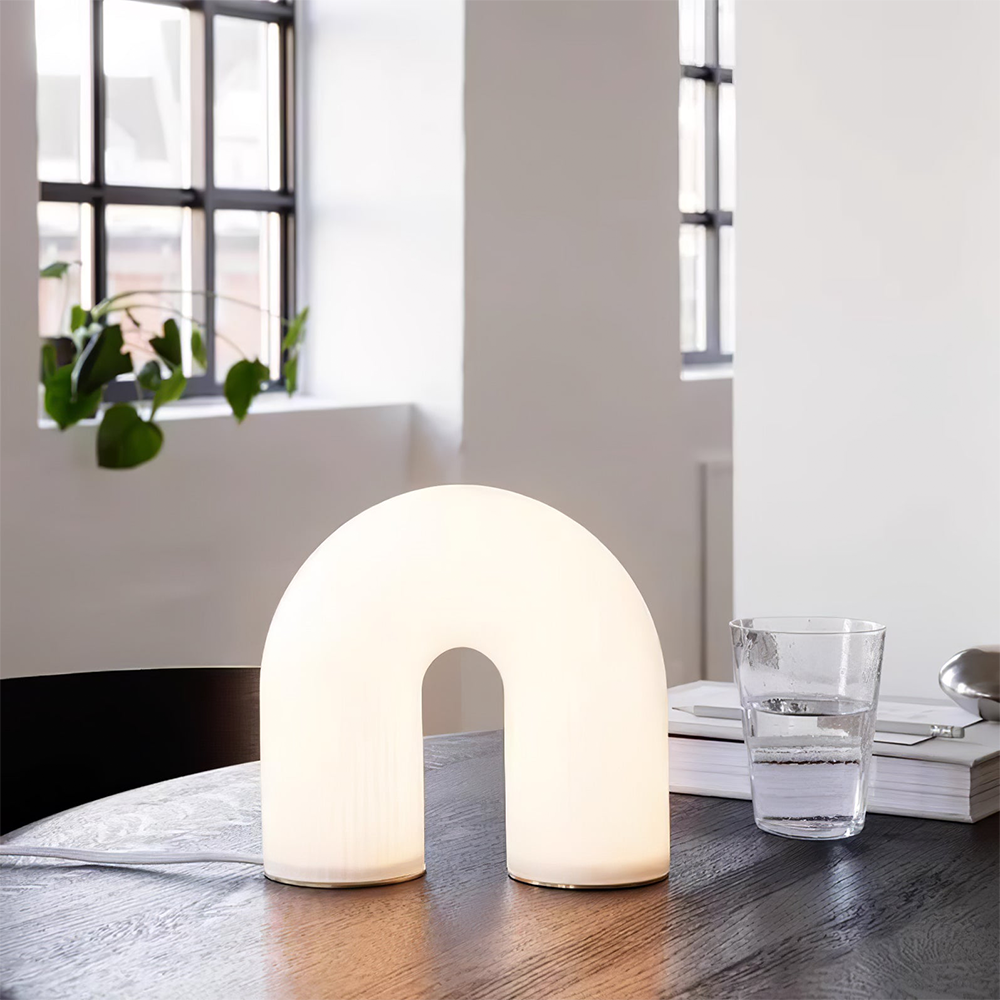 Arch lamp on a round dark wood table beside books and a water glass near black-framed windows