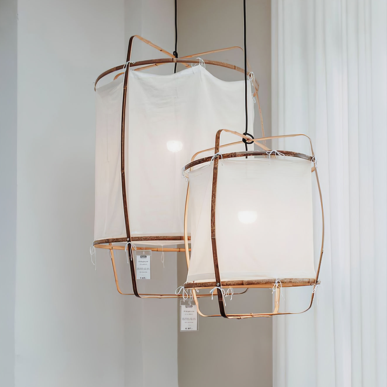 Two differently sized white fabric frame lamps before white curtains with hanging tags