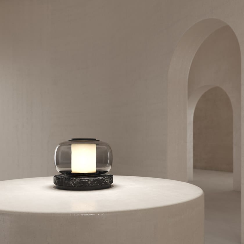 Smoke-grey glass lamp with a glowing cylindrical centre and dark veined base on a pale round table in a beige room with arched recesses