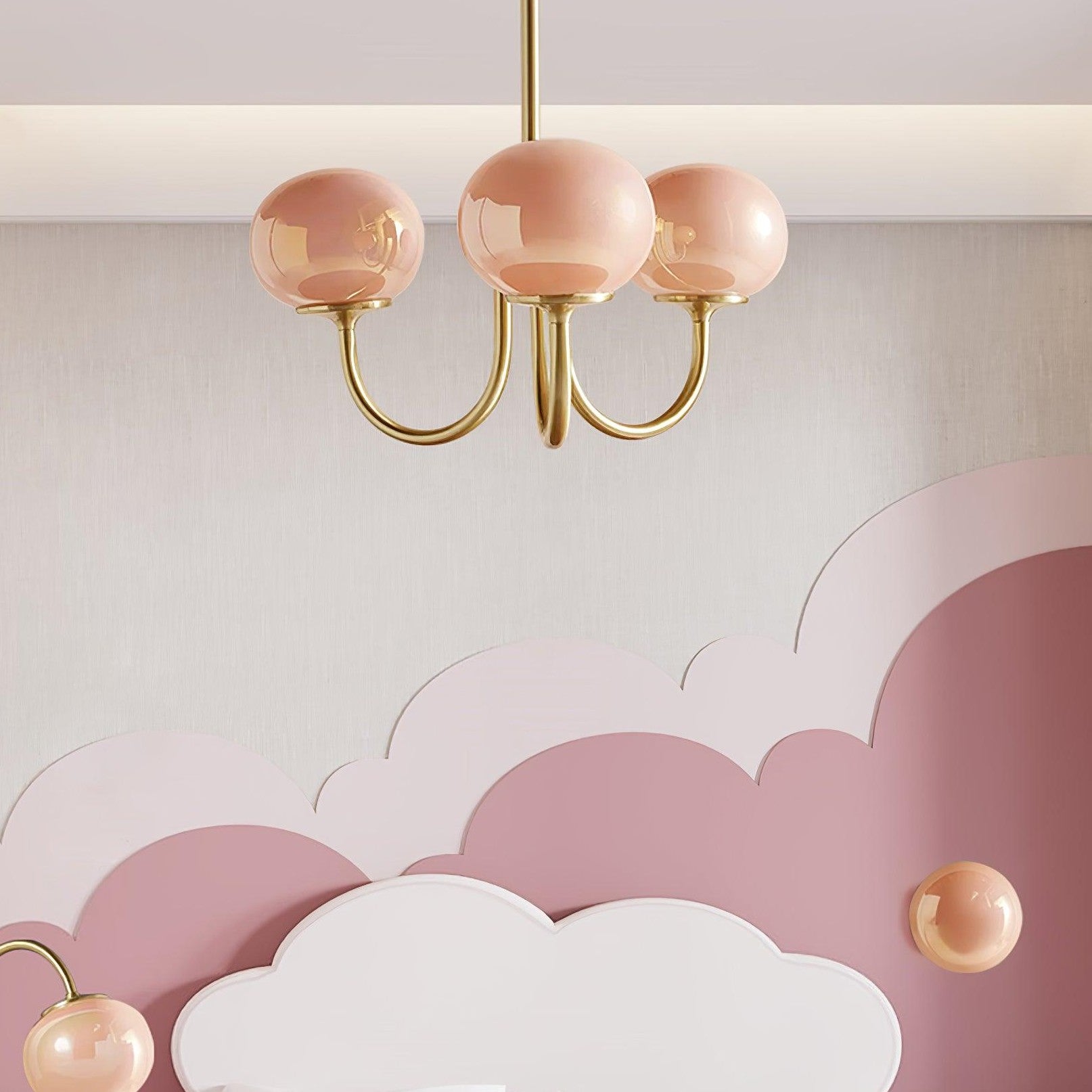 Pink three-globe chandelier above a scalloped pink-and-white headboard, with separate small lamps below