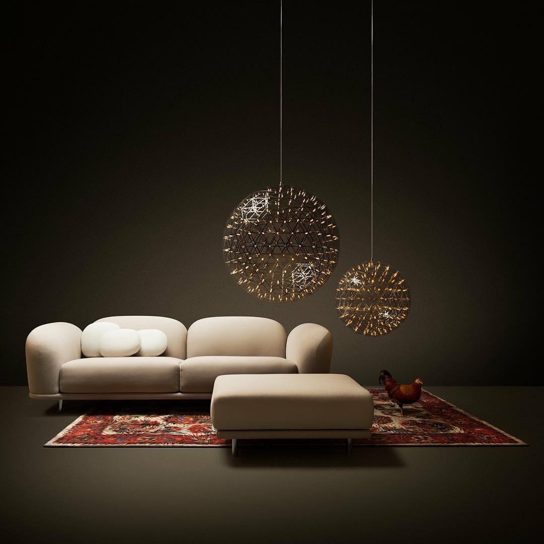 Two lattice spheres above cream sofas and an ottoman with a red rug below