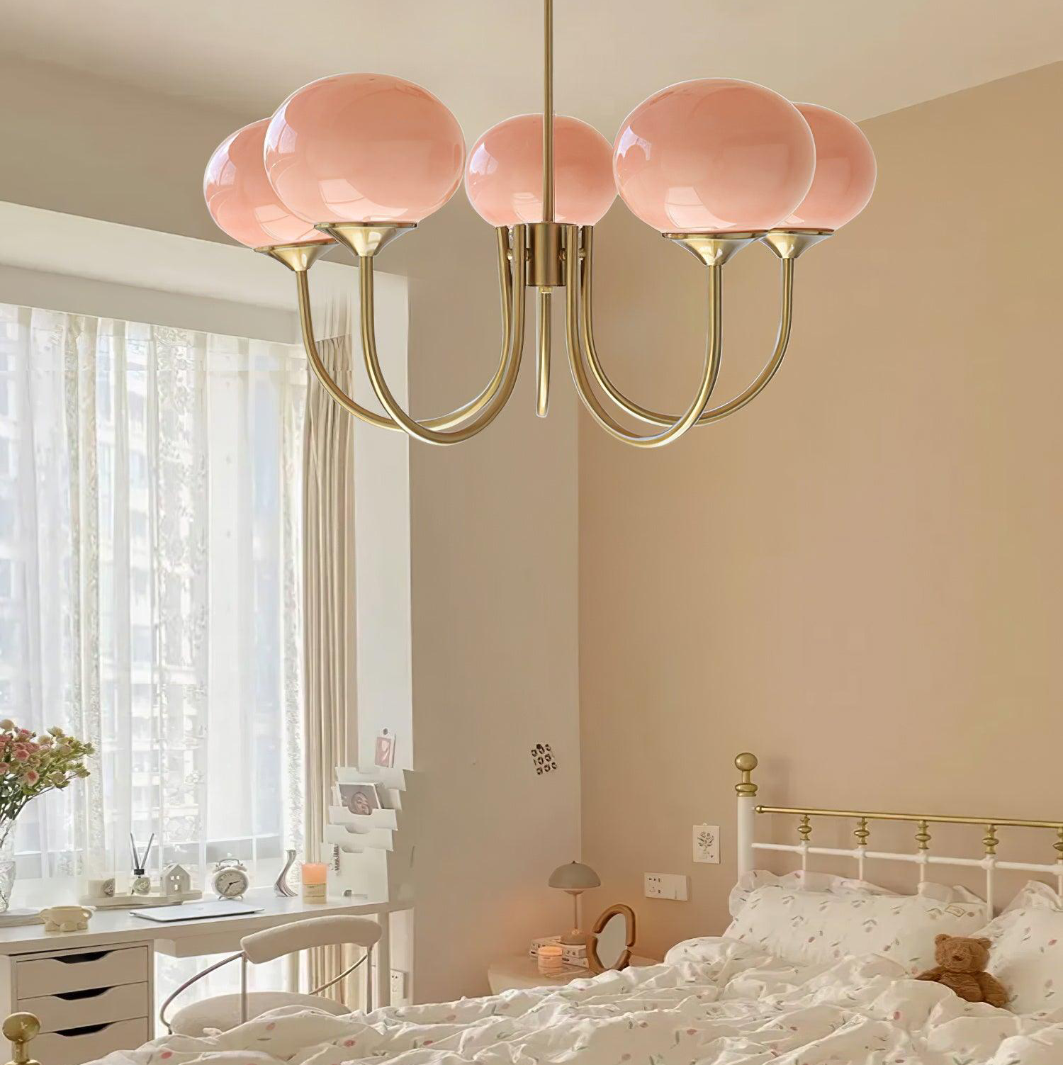 Five pink glass globes on gold-tone curved arms in a bedroom beside a window