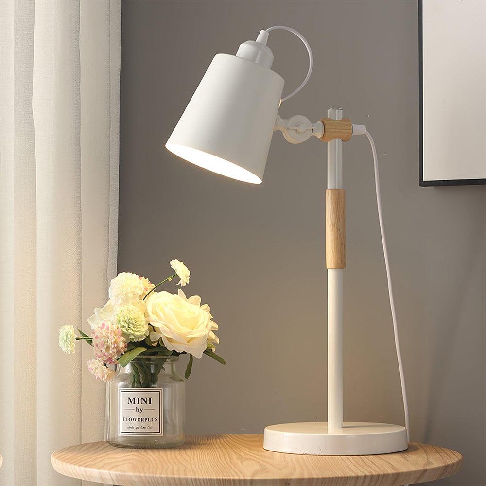 Lit White table lamp with wood details on round wooden table beside flower vase, pale curtain and framed art