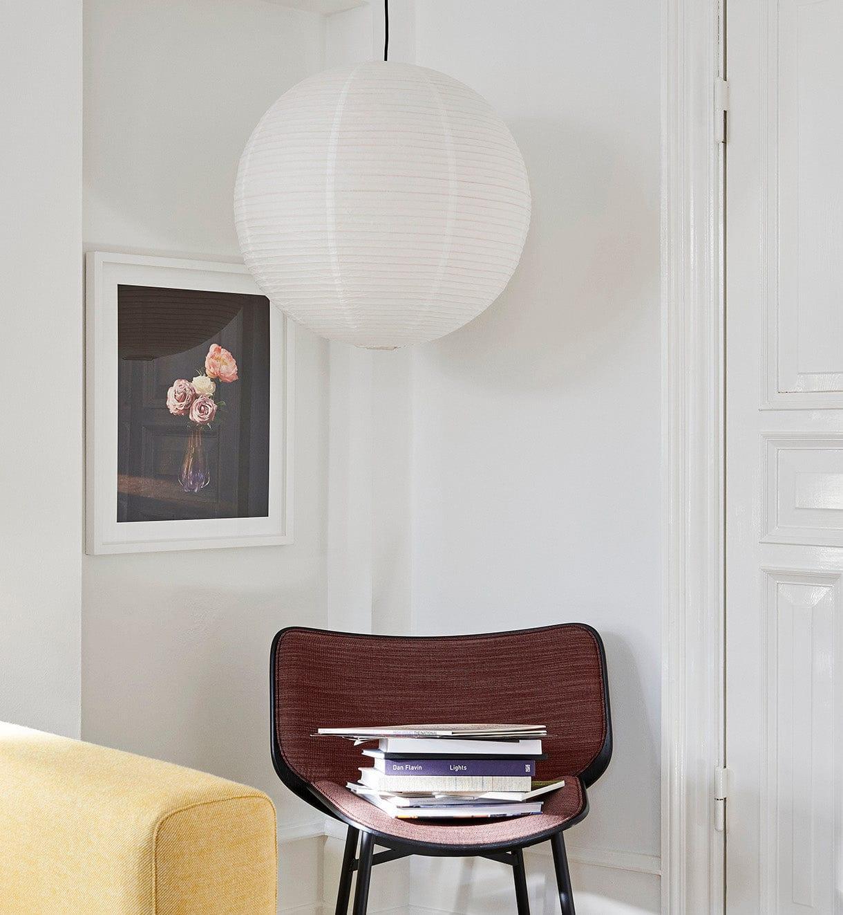 Paper globe above a maroon woven chair and books beside a yellow sofa and framed flower print