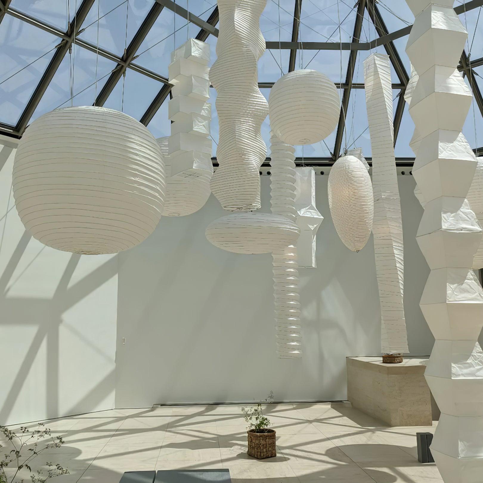 Globe, flattened, twisted and faceted paper shades hanging in a glass-roof exhibition space