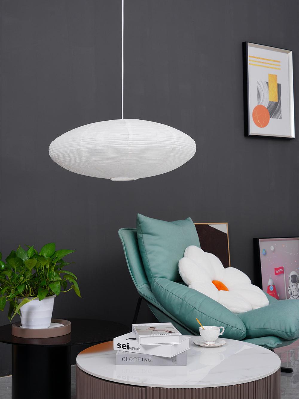 Flattened White shade above a teal lounge chair with a flower cushion, books, cup and framed artwork