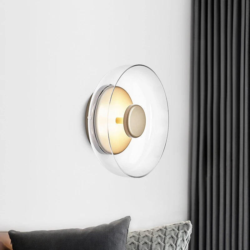 Clear bowl wall light above gray cushions beside a dark curtain