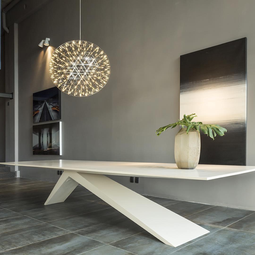 Single open-sphere pendant above a white table with a tall vase and monochrome artwork