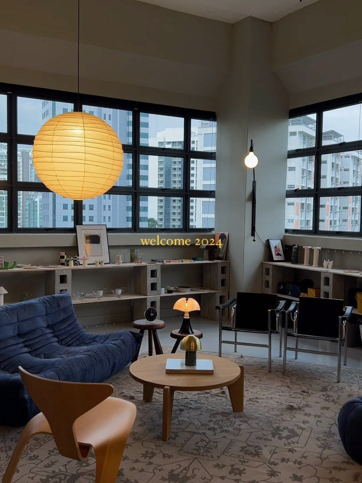 Glowing paper globe above a blue sofa and round wood table in a room with industrial windows and shelving