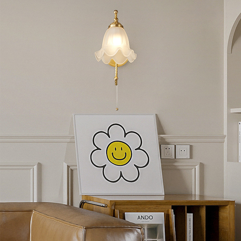 Front view of petal wall light with hanging chain above smiley-flower print, wooden bookcabinet and brown chair
