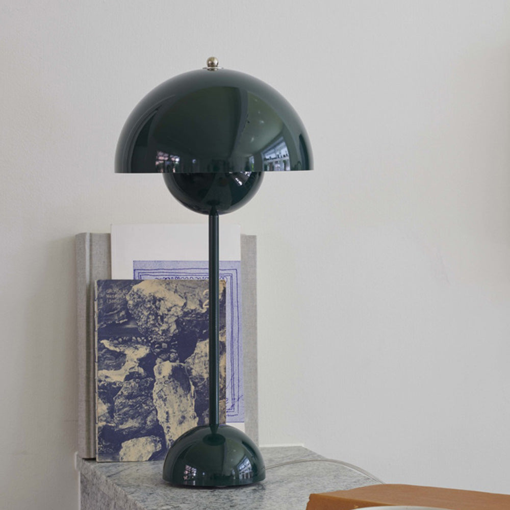 Green dome lamp on a grey ledge beside upright books, with a pale cable behind the base