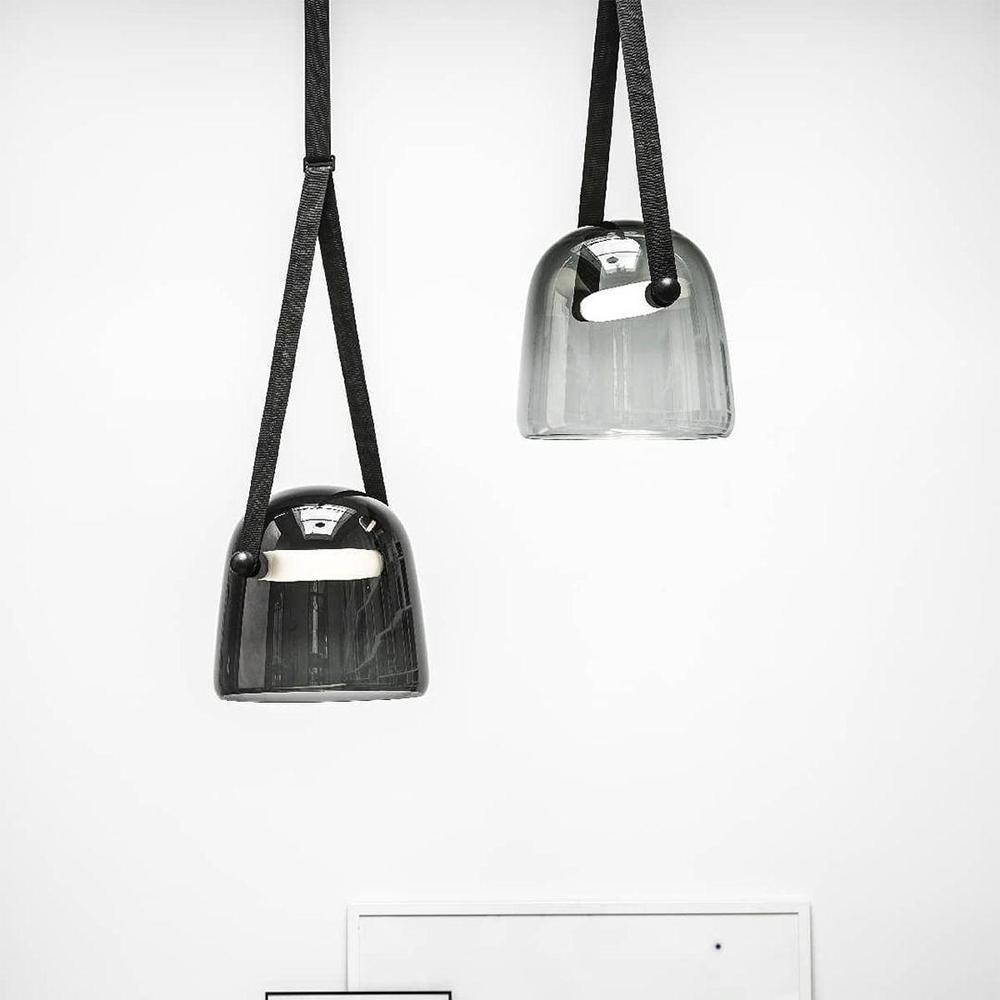 Two smoked glass pendants with black split straps hanging at different heights against a white wall