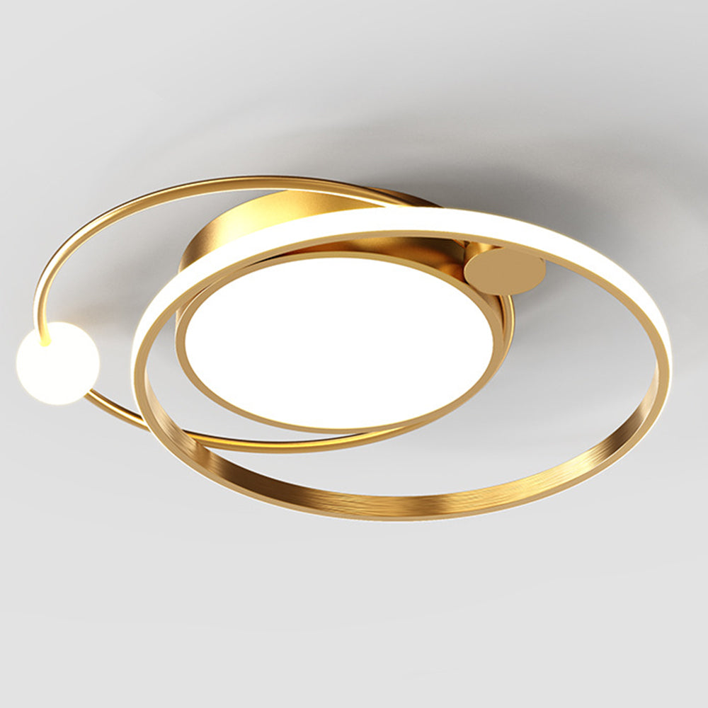 Gold-tone orbital ceiling fixture illuminated against a pale ceiling with central disk and sphere-ended loop