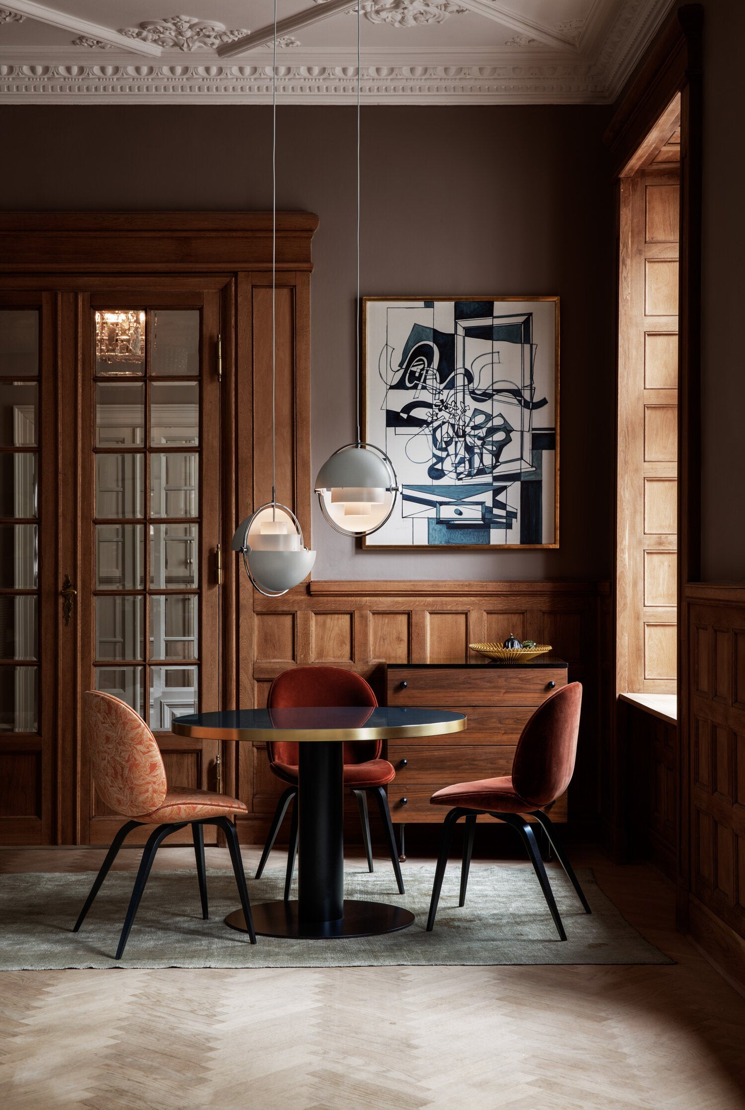 Two pale ring pendants in a wood-panelled room with red dining chairs.
