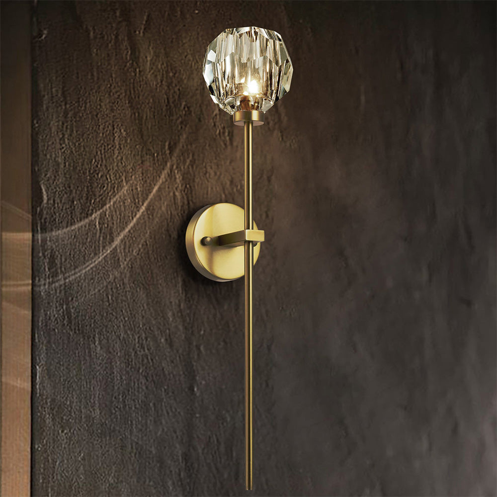 Lit clear faceted ball with gold-tone rim and long stem against a textured dark wall