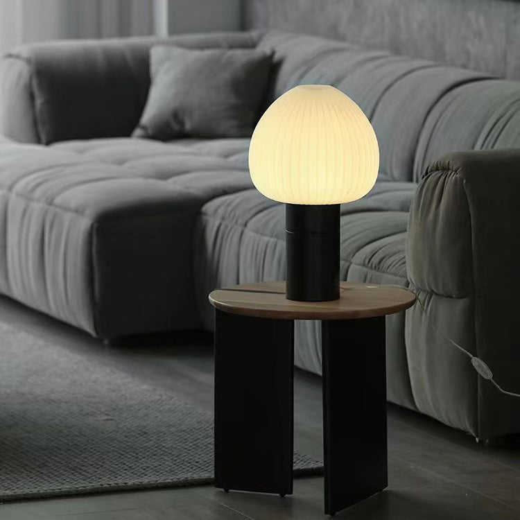 Glowing ribbed-shade lamp on a wooden side table beside a grey sofa and cushions, with cable visible at the side