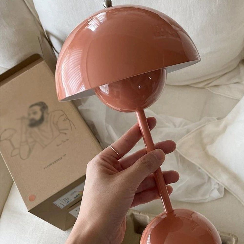 Hand holding the stem of a glossy pink dome table lamp over white bedding