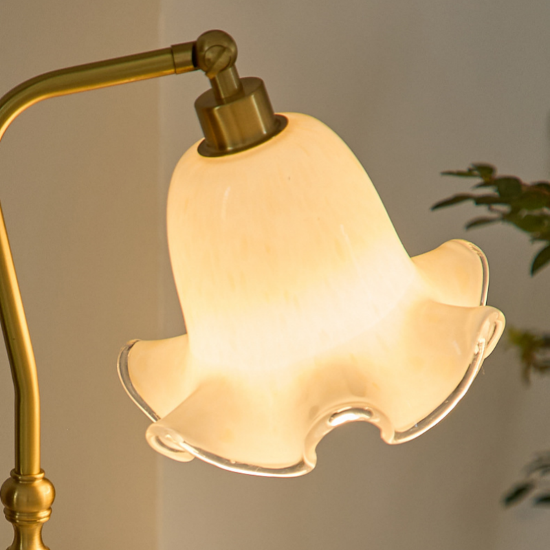 Close-up of glowing cream flower-shaped shade with clear wavy rim, gold-toned joint and curved arm