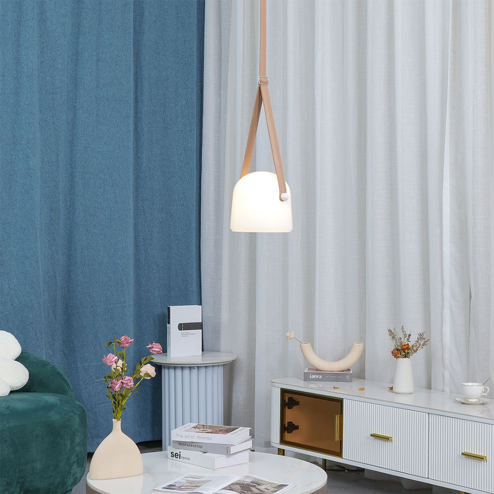 Opaque white bell-shaped pendant with tan strap beside white curtains, blue wall and green sofa