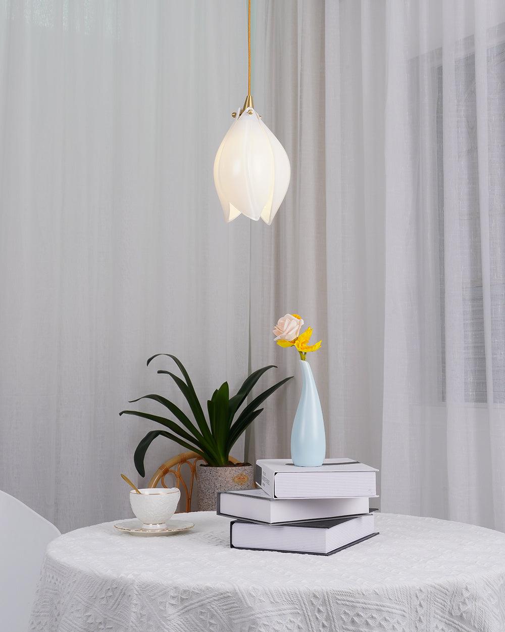 Glowing white flower bud over a blue vase, books and cup beside a plant