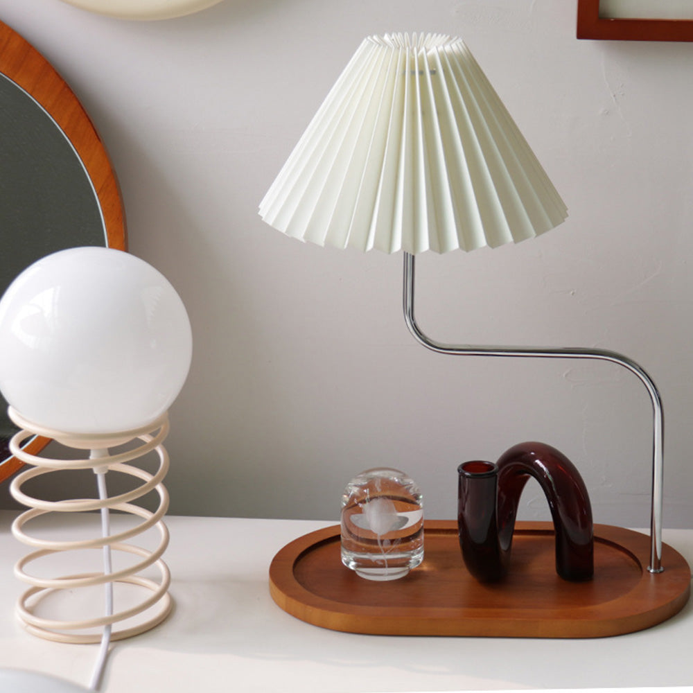 Pale pleated shade on an offset metal stem above a wood tray-like base beside a separate globe lamp
