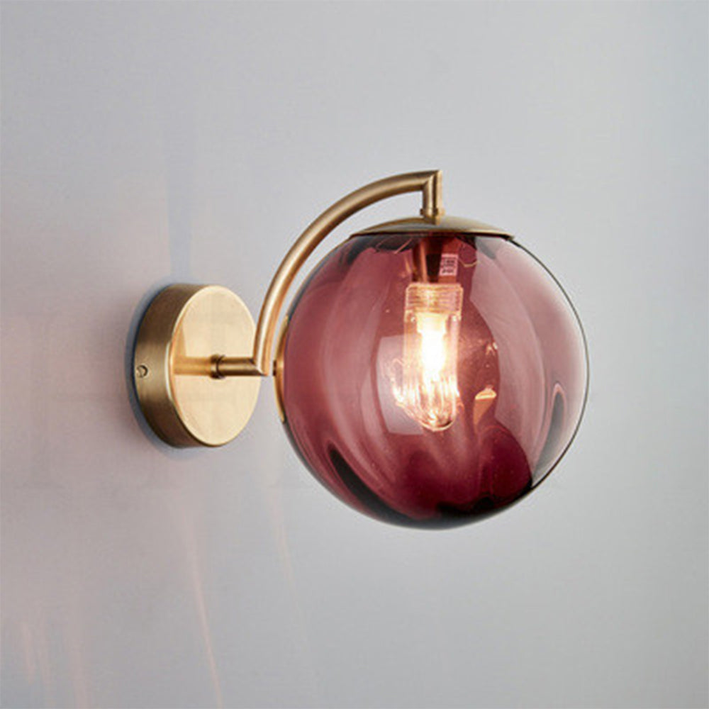 Red tinted globe wall light with a glowing bulb, curved gold-tone arm and round plate on a pale wall