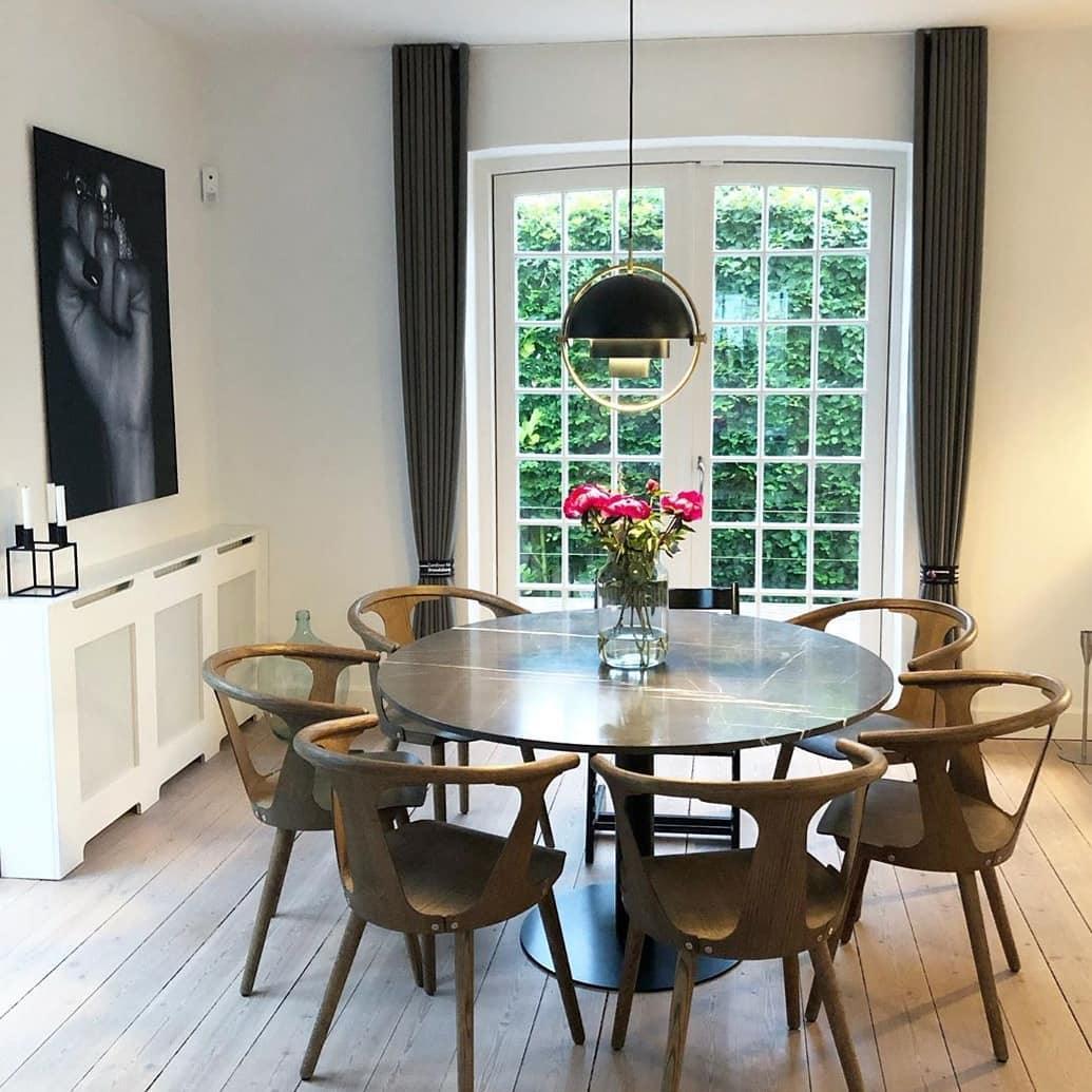 Black dome pendant above a round glass dining table near a window.