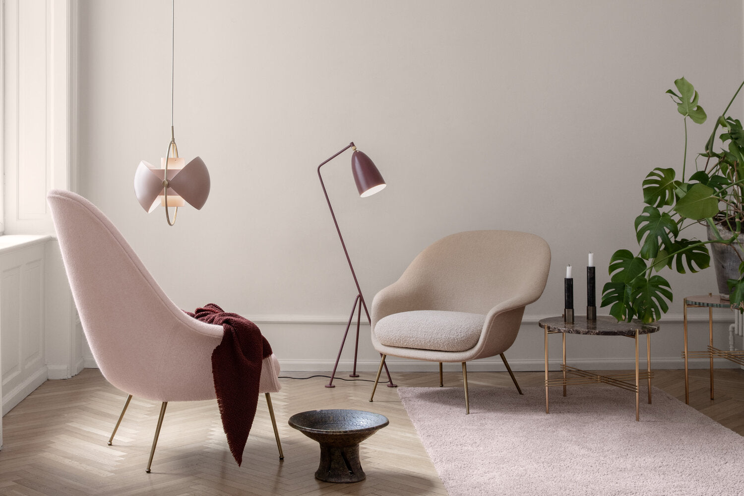 Pink adjustable pendant with open shade halves beside pale lounge chairs.