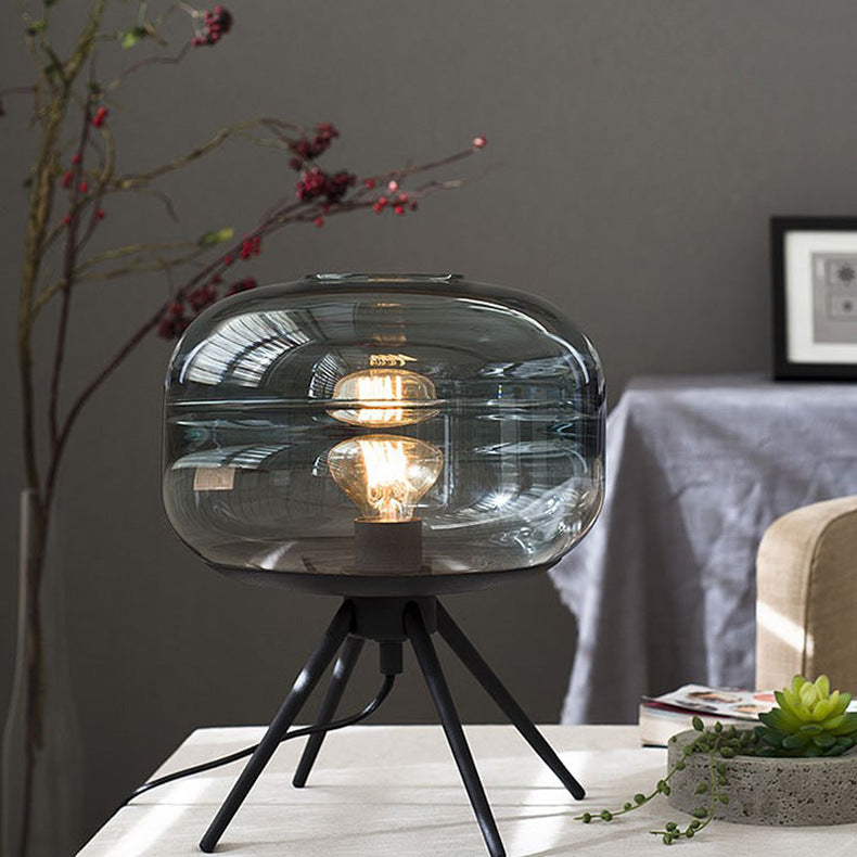 Lit blue-tinted glass lamp with a reflected bulb above black legs beside a succulent pot and books on a pale table