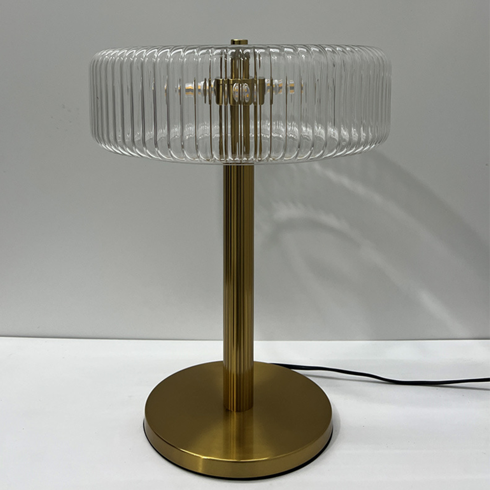 Unlit clear ribbed-glass lamp with visible centre fittings, a gold-tone column, circular foot and black cord extending right